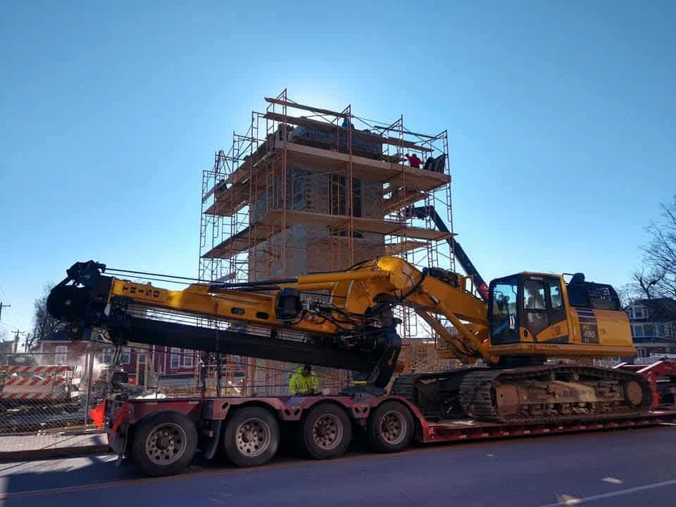 A large tracked excavator staged in front of a multi-story scaffolding setup for a concrete block masonry Indianapolis tower build.