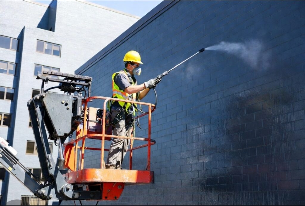 Technician performing masonry waterproofing Indianapolis service on exterior brick building.