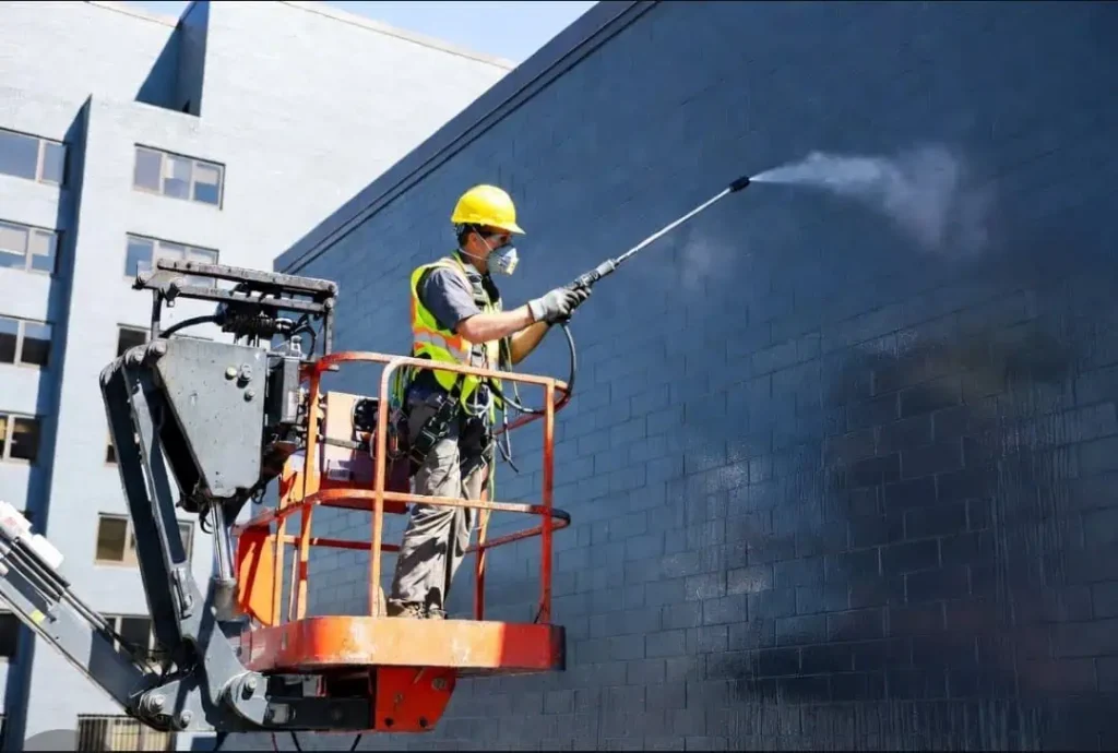 A certified masonry technician from Emerson Masonry Inc in a boom lift applies penetrating sealant for comprehensive masonry waterproofing in Indianapolis on a commercial brick building for Emerson Masonry Inc.